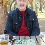 Senior man sitting outdoors in a park playing checkers on a sunny day.